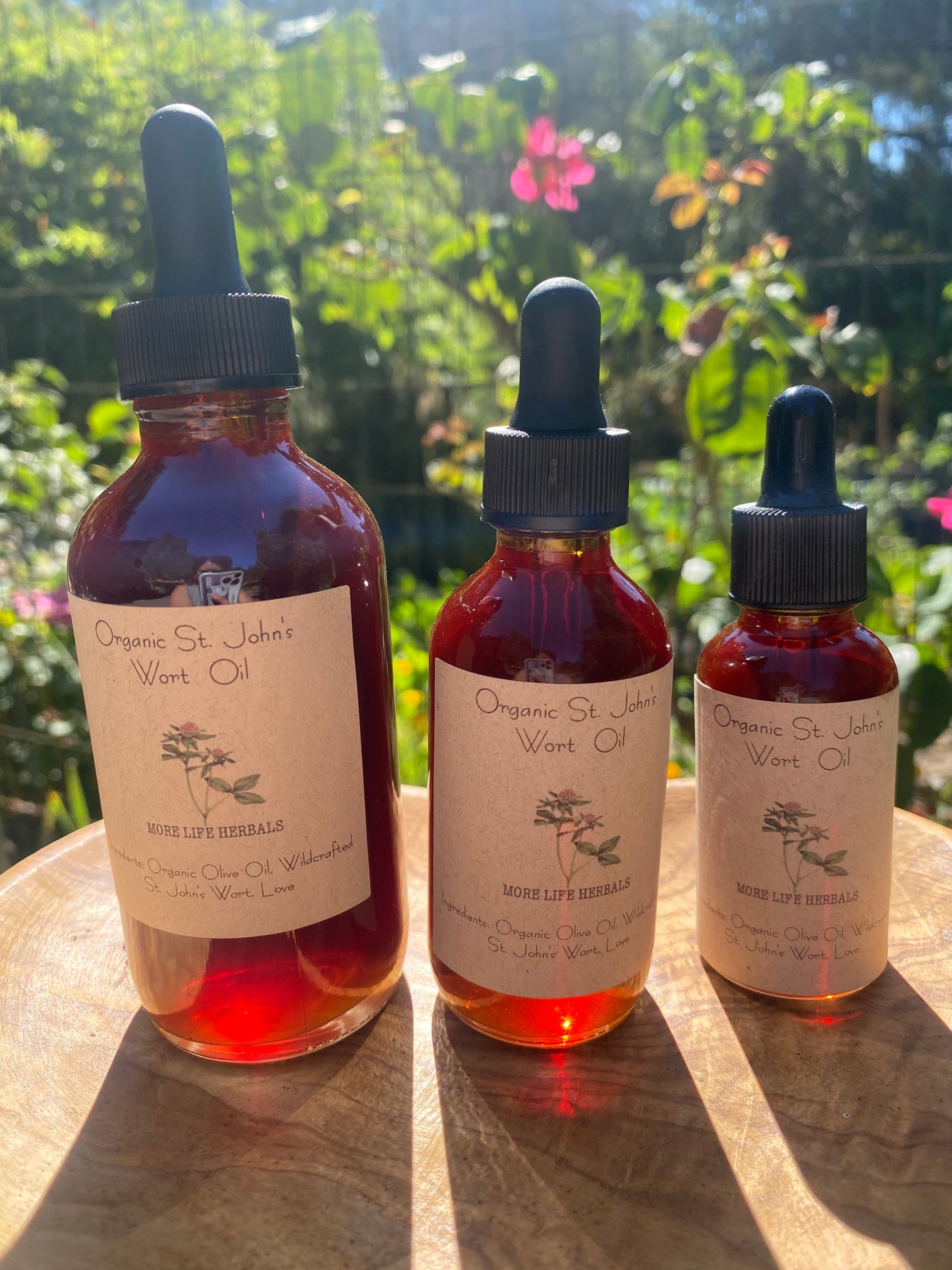Three Bottles of St. John's Wort Oil with labels on a wooden surface with greenery and flowers in the background