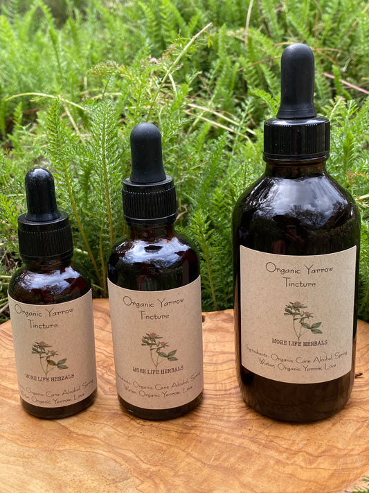 Three bottles of Organic Yarrow Tincture on a wooden surface with greenery in the background